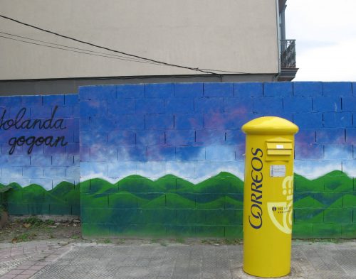 yellow postbox in front of painted mountain panorama