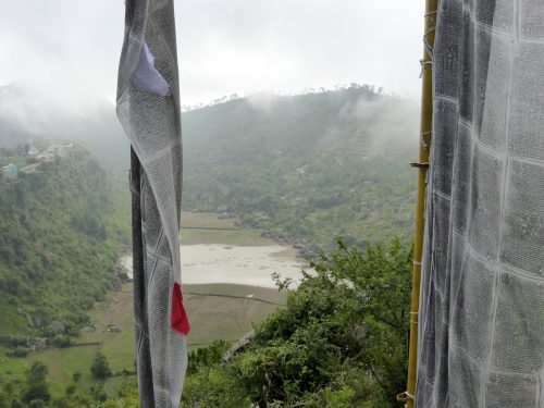 misty lake between prayer flagpoles