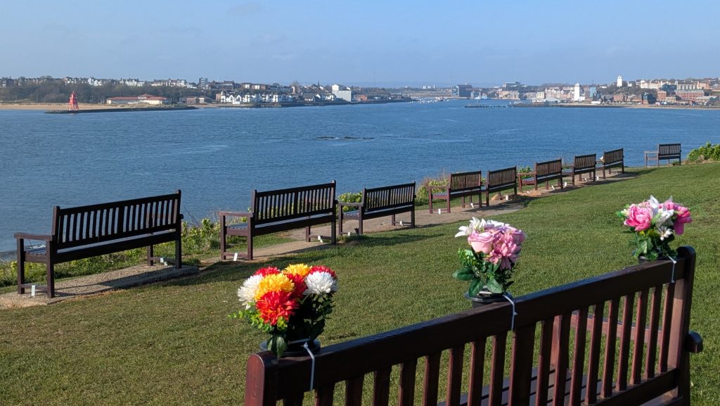 sunlight catches memorial flowers on benches looking down the Tyne